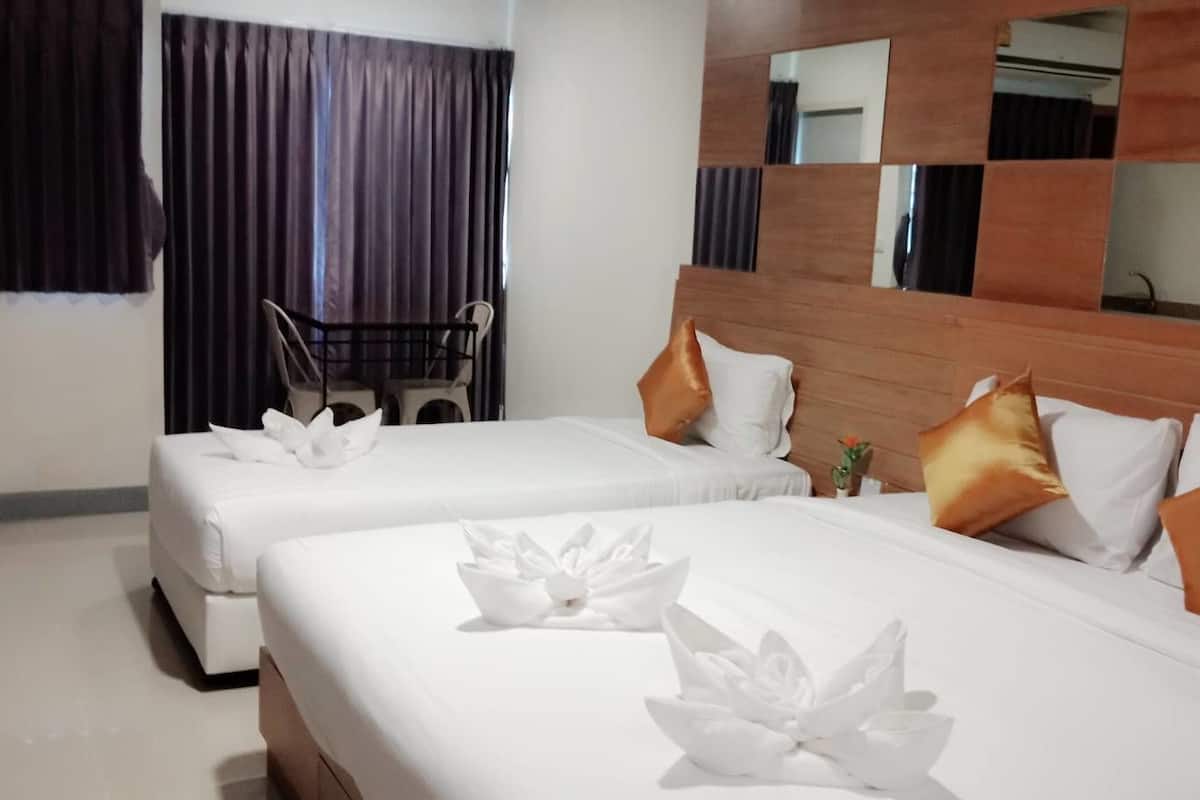 Habitación de hotel con dos camas, cada una con ropa de cama blanca y almohadas decorativas. Cuenta con un cabecero de madera y un espejo grande sobre las camas.
