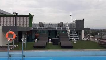 A rooftop pool area with lounge chairs and a lifebuoy, a staircase, and a view of the city.
