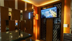 A modern hotel room with a glass coffee table, wooden paneling, a mounted TV, and a decorative partition. - The Greenery Central Suites (San Sai)