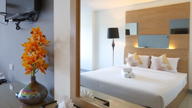 A hotel room with a bed, a TV mounted on the wall, and a vase with flowers on a table. - The Greenery Central Suites (San Sai)