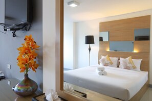 Una habitación de hotel con una cama, un televisor montado en la pared y un jarrón con flores sobre una mesa.