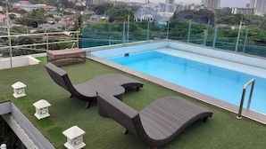 A rooftop pool with wicker loungers and a view of the cityscape. - The Greenery Central Suites (San Sai)