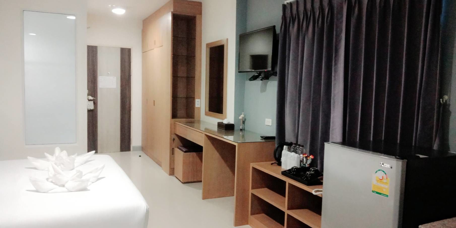 A hotel room with a bed, a desk, a mirror, a TV, and a refrigerator.