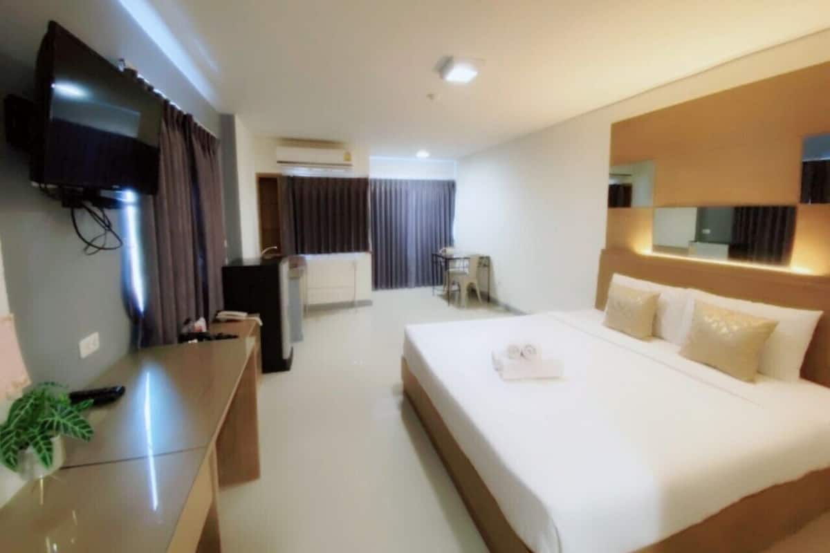 Habitación de hotel con una cama grande, un escritorio con computadora, un televisor de pantalla plana en la pared y una mesita con una silla.