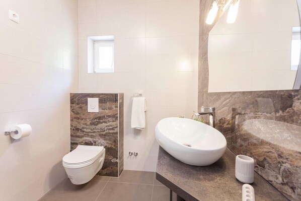 Ein modernes Badezimmer mit Marmorwaschtisch, weißem Waschbecken und Toilette.
