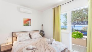 Een slaapkamer met een bed, een gitaar, een hoed en een raam met uitzicht op zee.