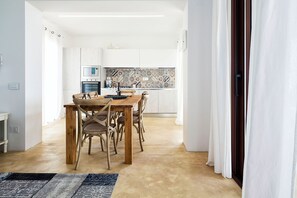A modern kitchen with white cabinets, a tiled backsplash, and a dining area with a wooden table and chairs.