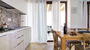 A kitchen with a tiled backsplash, a wooden dining table with chairs, and a bottle of wine on the table. - Lavanda - Front Sea Villa for 8 People with Pool (Reitani)