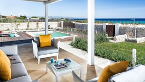 A covered outdoor seating area with a pool, a stone wall, and a view of the sea. - Lavanda - Front Sea Villa for 8 People with Pool (Reitani)