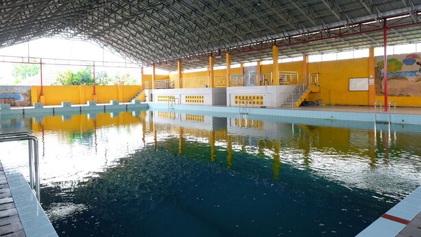 Ein überdachter Schwimmbereich mit hoher Decke, gelben Wänden und freiem Blick auf das Becken.