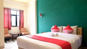 Ein Hotelzimmer mit einem großen Bett, zwei Stühlen, einem kleinen Tisch und einem Fenster mit Vorhängen.