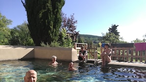 Ein klarer Außenpool mit Schwimmern, umgeben von einer Holzterrasse und viel Grün.