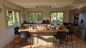 Una cocina moderna con una isla grande, dos sillas negras, un refrigerador y vistas al exterior.