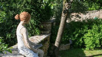 A statue of a woman seated on a stone bench in a garden with stone walls and lush greenery.