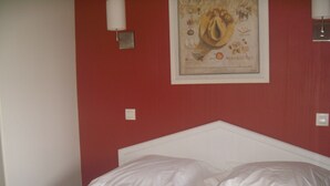 Una cama con sábanas blancas en una habitación con paredes rojas.