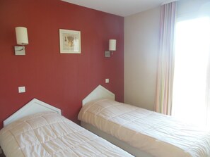 Une chambre avec deux lits, un mur rouge et une fenêtre avec des rideaux.