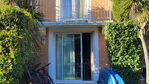 Una casa de dos pisos con un balcón, una puerta corrediza de vidrio y un patio con mesa y sillas.