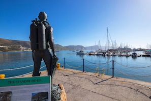 Una statua di un sub con un cartello intitolato 'The Standby Diver' vicino a un porto turistico con barche.