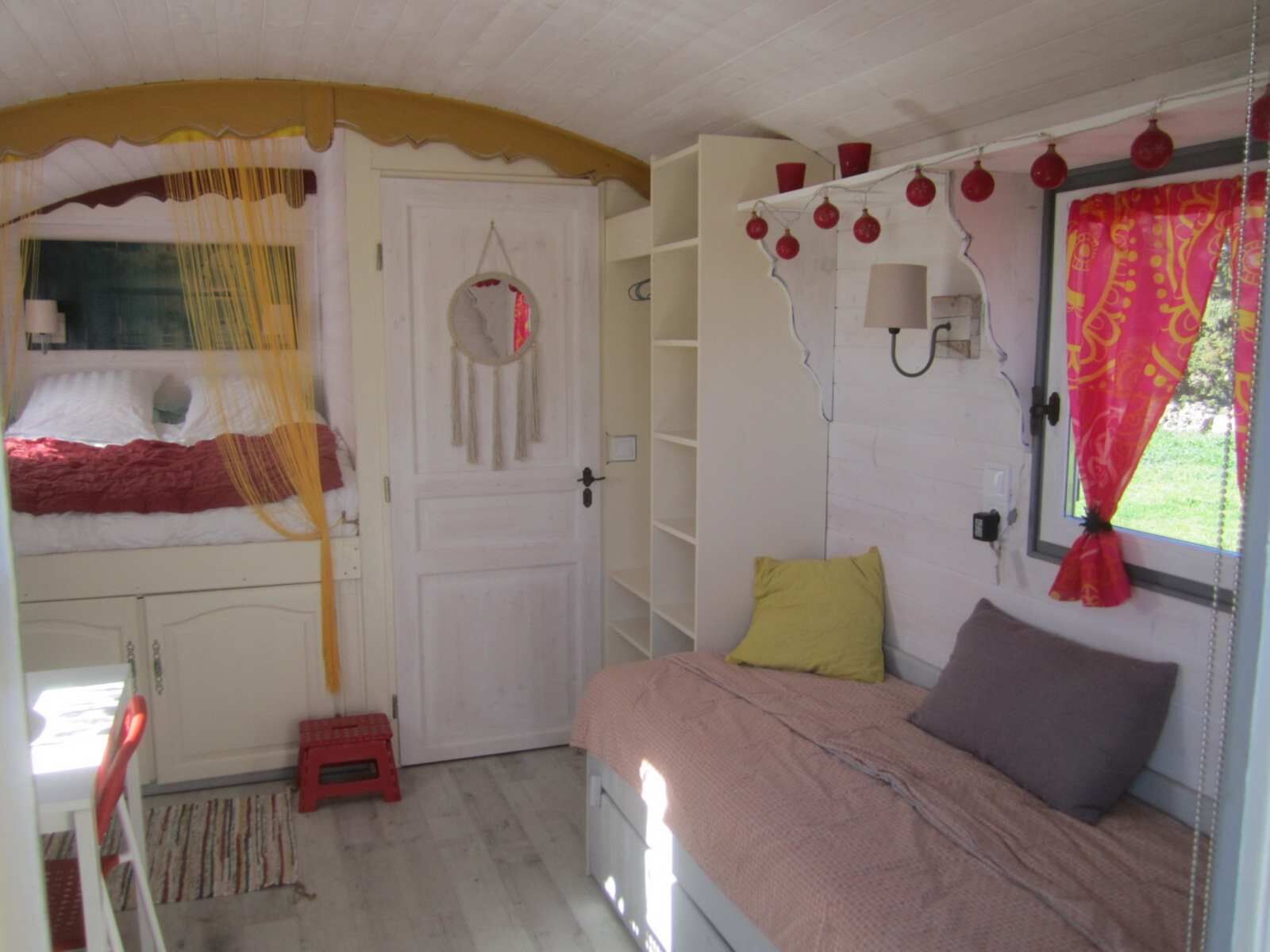 Une chambre à coucher avec un lit, une armoire, un petit tabouret et une fenêtre avec des rideaux.
