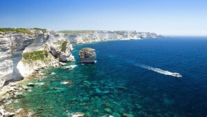 A coastal landscape with clear blue waters, rocky cliffs, and a boat in motion. - House 150 meters from the beach PALOMBAGGIA private access (PORTO VECCHIO)