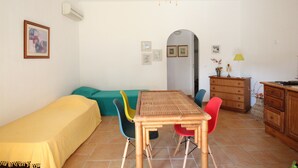A small, well-lit room with a bed, a dining table with chairs, a dresser, and a wall-mounted air conditioner. - House 150 meters from the beach PALOMBAGGIA private access (PORTO VECCHIO)