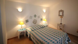 A bedroom with a bed, two bedside tables with lamps, a wall-mounted mirror, and decorative wall art. - House 150 meters from the beach PALOMBAGGIA private access (PORTO VECCHIO)