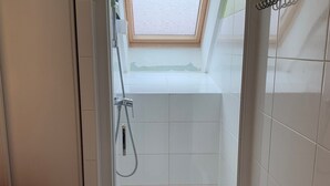 Un espace douche avec un puits de lumière, des carreaux blancs et une serviette rouge posée sur une chaise.