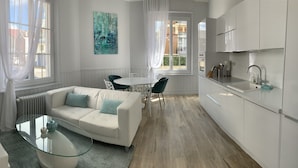 Una cucina moderna con mobili bianchi, una zona pranzo con tavolo e sedie bianche e un soggiorno con divano bianco e tavolino in vetro.