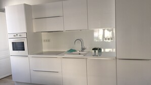 Una cucina moderna con mobili bianchi, forno integrato, lavello e rubinetto in acciaio inossidabile.