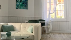 Un soggiorno moderno con un divano bianco, un tavolino in vetro e un tappeto verde. C'è un quadro appeso al muro e una finestra con tende.