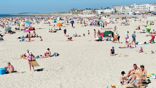 Una spiaggia affollata con persone che prendono il sole e nuotano.