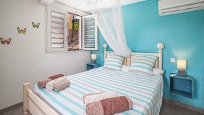 A bedroom with a bed, nightstands, a window with shutters, and a mosquito net.
