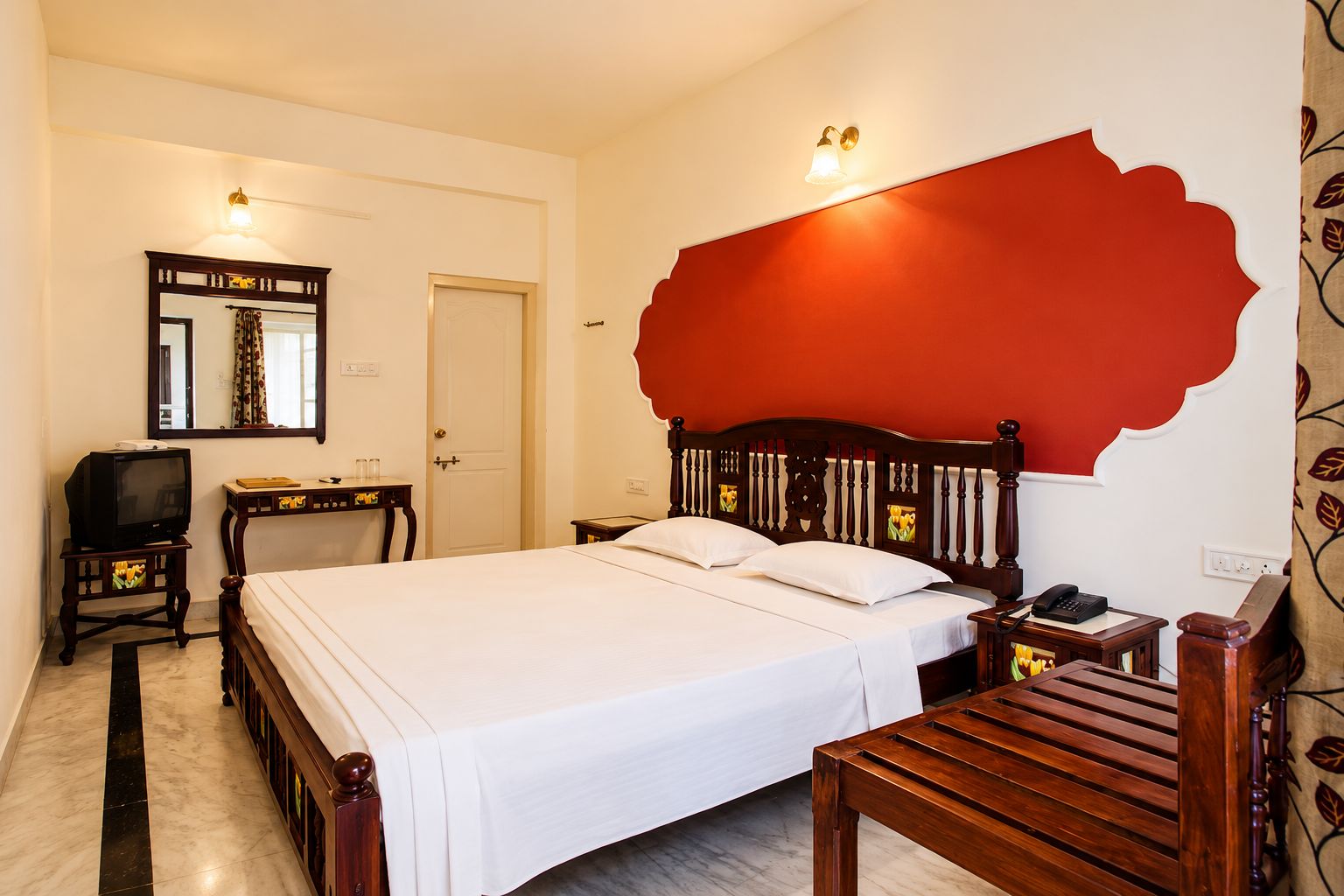 Habitació d'hotel amb llit, taula de nit, escriptori petit amb televisió i una paret vermella decorativa.