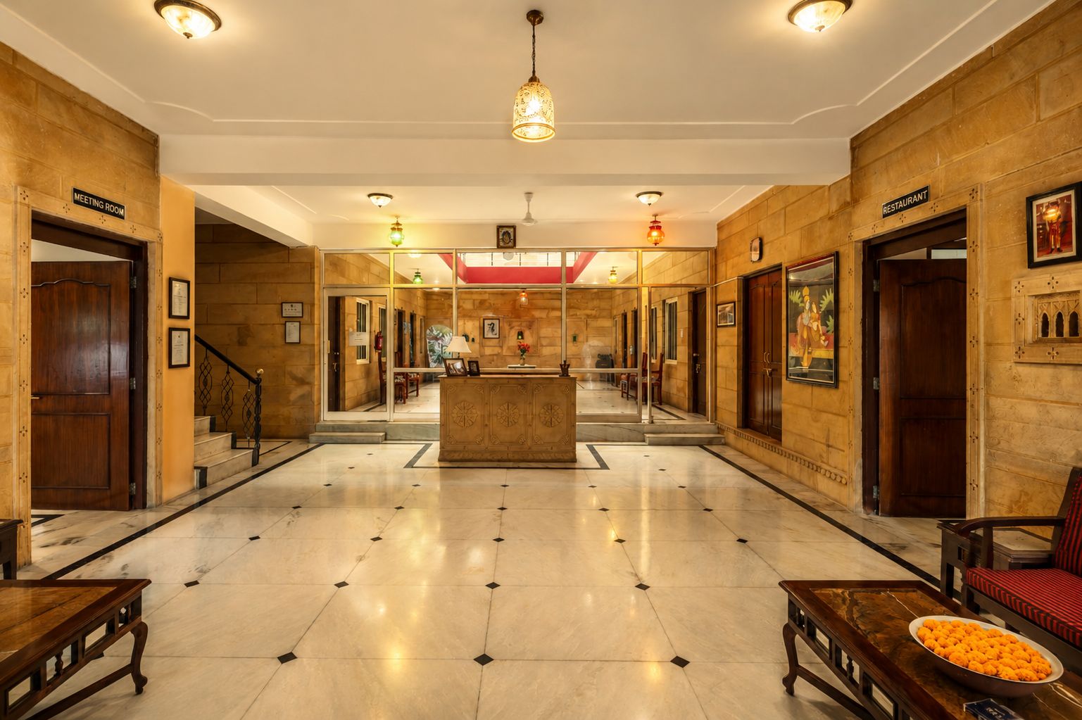 Un hall de hotel con mostrador de recepción, una escalera y puertas que dan acceso a la sala de reuniones y al restaurante.