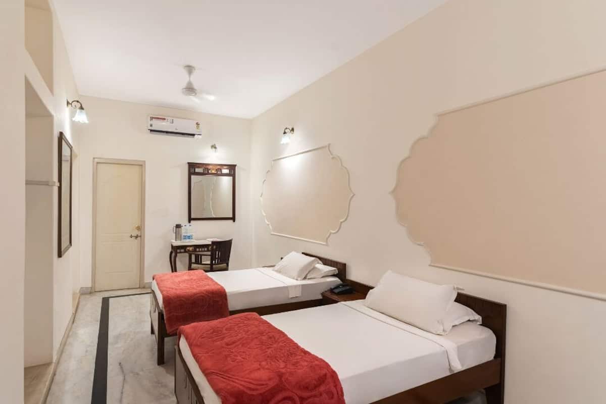 A hotel room with two beds, a desk, a chair, a mirror, and a ceiling fan.
