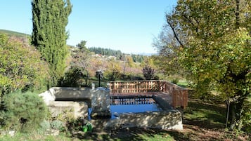 Ein Garten mit Brunnen, einer Holzterrasse und Blick auf die umliegende Landschaft.
