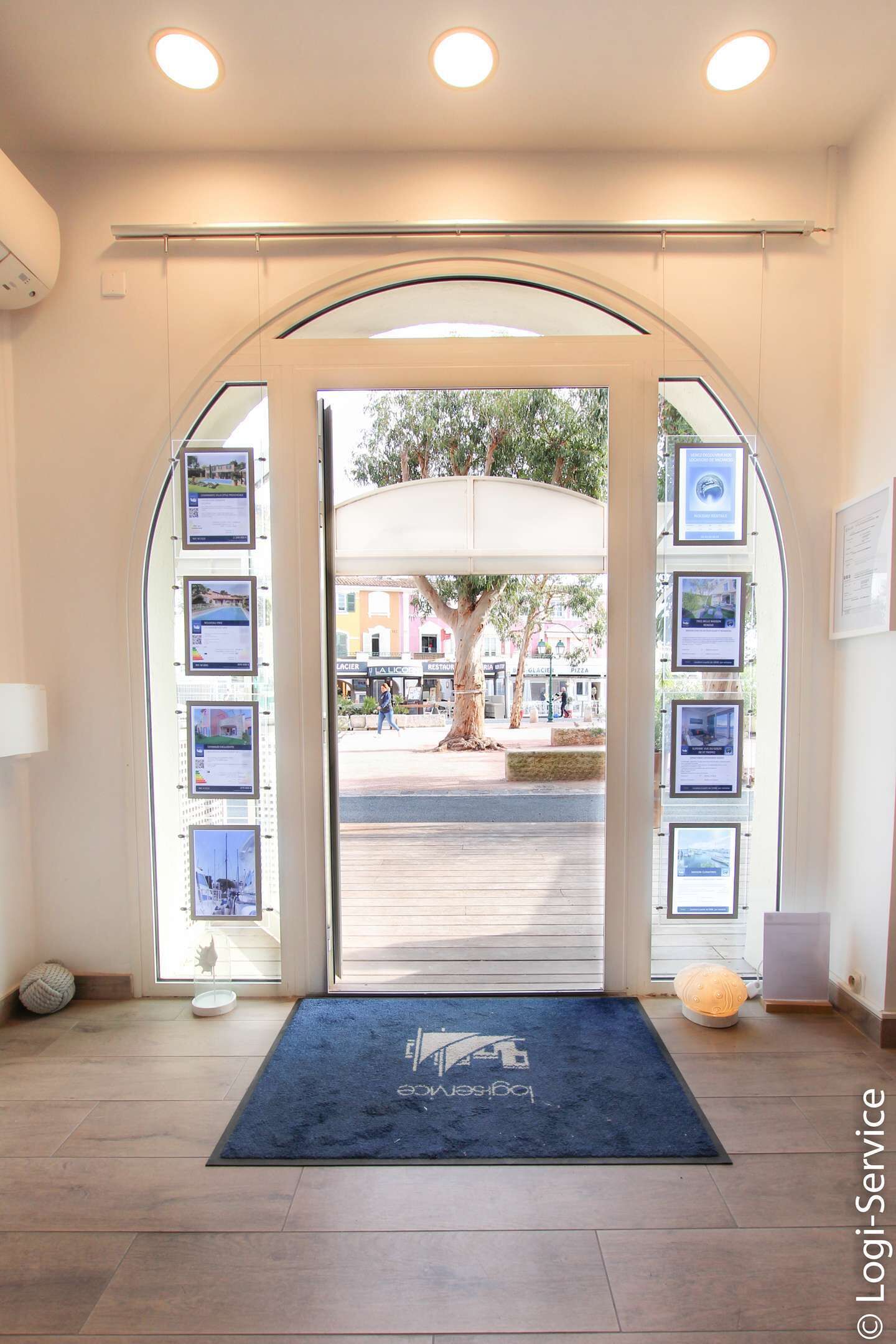 An entrance with a blue mat, framed pictures on the walls, and a view of the street outside.