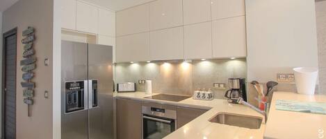 Una cocina moderna con electrodomésticos de acero inoxidable, horno empotrado y una isla grande con fregadero.
