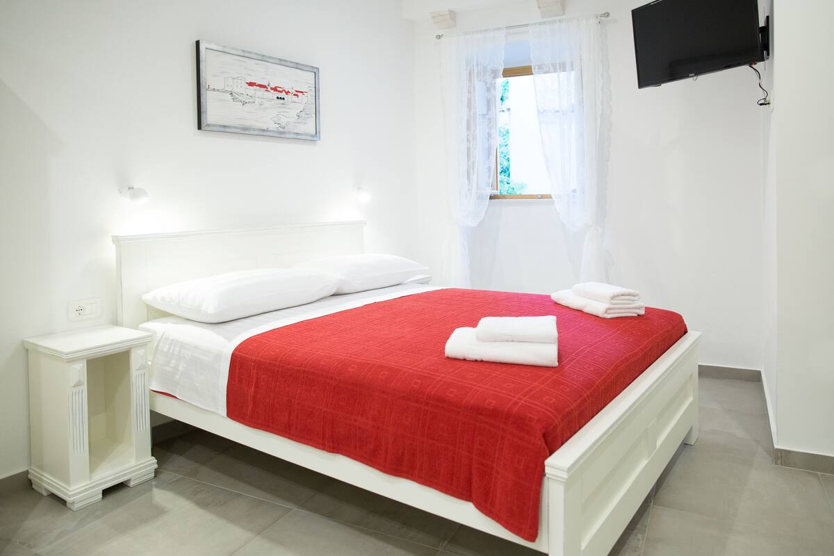 Un lit bien fait, avec une couverture rouge, des oreillers blancs et des serviettes pliées.