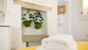 A bathroom with a yellow towel on a counter, a white sink, and two green plants hanging from a shelf. - Dubrovnik old city Studio apartment (Dubrovnik)