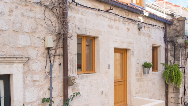 A narrow stone building with a wooden door, a potted plant, and a small staircase leading to a second floor. - Dubrovnik old city Studio apartment (Dubrovnik)