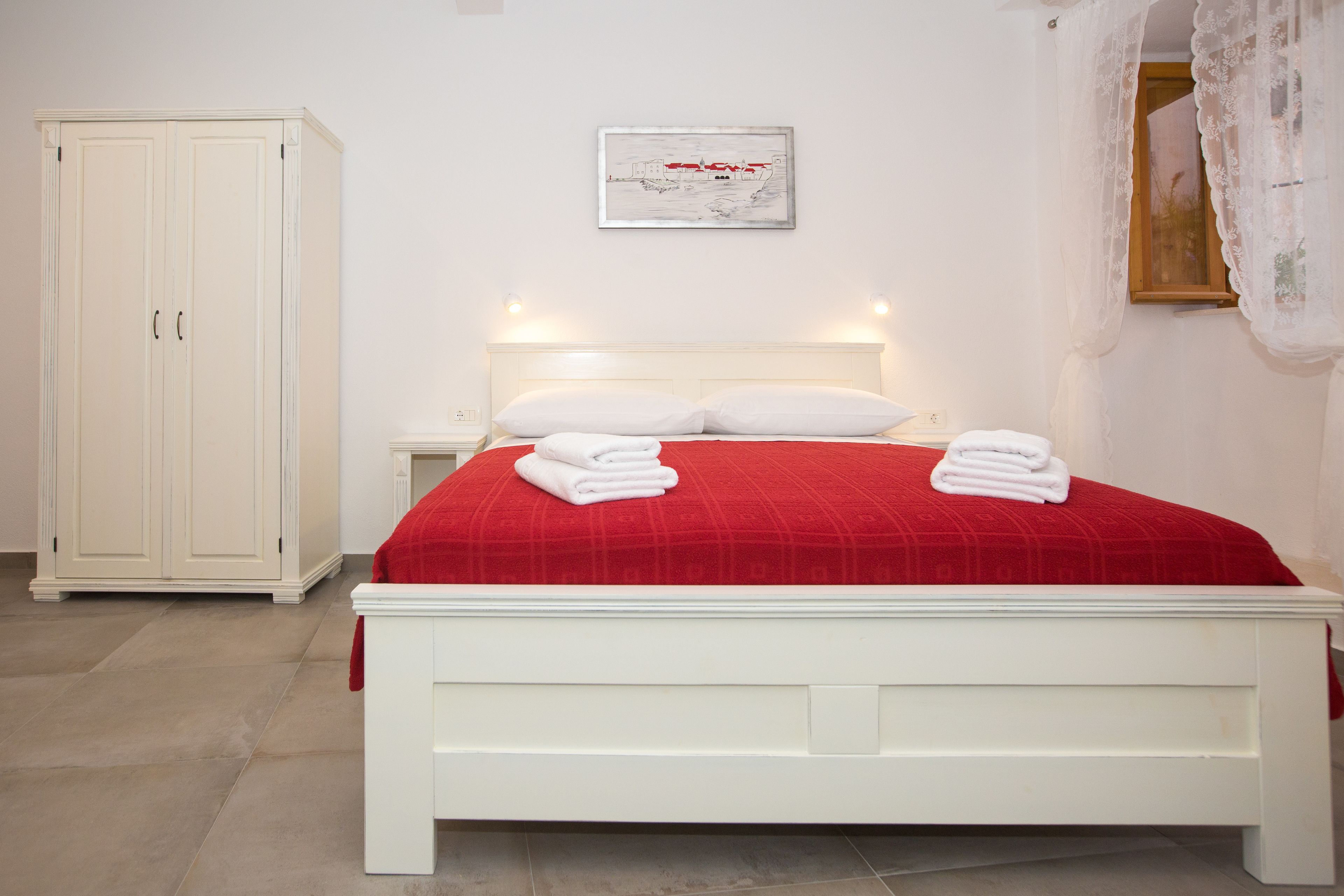 A bedroom with a bed, white wardrobe, and a framed picture on the wall.