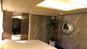 Quarto de hotel moderno com cama grande, planta em vaso, espelho de parede único e luminária no teto.