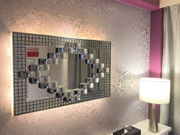 A bathroom with a large mirror, a wall-mounted air conditioner, and a bedside table with a lamp.