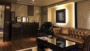 Uma sala de estar moderna com um sofá de couro, uma mesa de centro de vidro e uma área de cozinha com armários de madeira escura e um micro-ondas.
