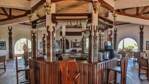 A wooden bar area with high ceilings and decorative columns, featuring a central bar counter and seating around it. - Olympe Du Bemaraha (Bekopaka)