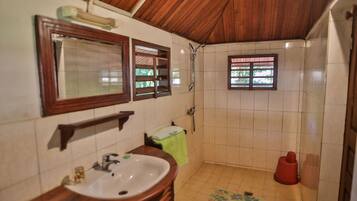 Un baño con techo de madera, un lavamanos, un espejo, una ducha y una ventana.