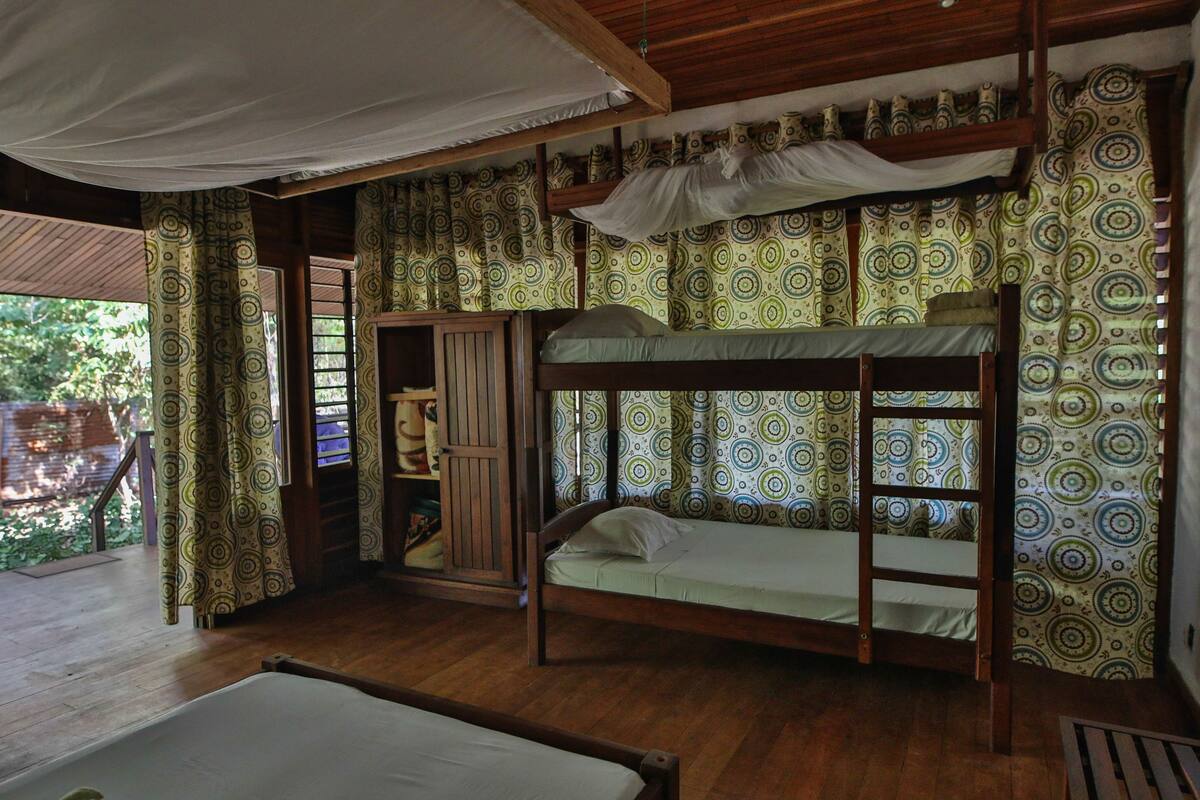 Ein Zimmer mit einem Etagenbett, Holzboden, gemusterten Vorhängen und einem Baldachin.