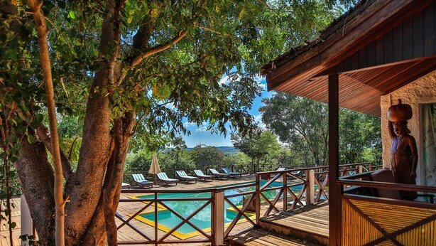 A pool area with a wooden deck, lounge chairs, and a view of trees and hills. - Olympe Du Bemaraha (Bekopaka)