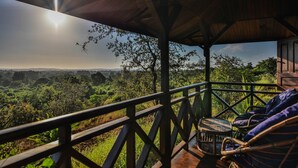 A wooden deck with a view of a lush landscape, a wooden railing, and a wicker chair. - Olympe Du Bemaraha (Bekopaka)